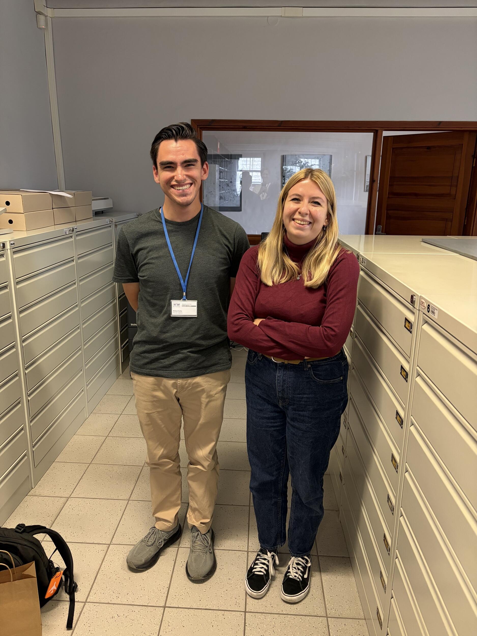 A photo of two people standing next to filing cabinets. 
