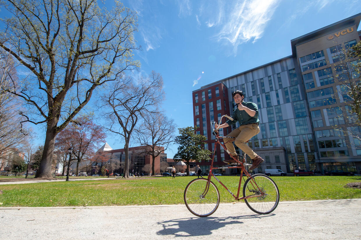 Man on tall bike riding through Monroe Park while giving the thumbs up.