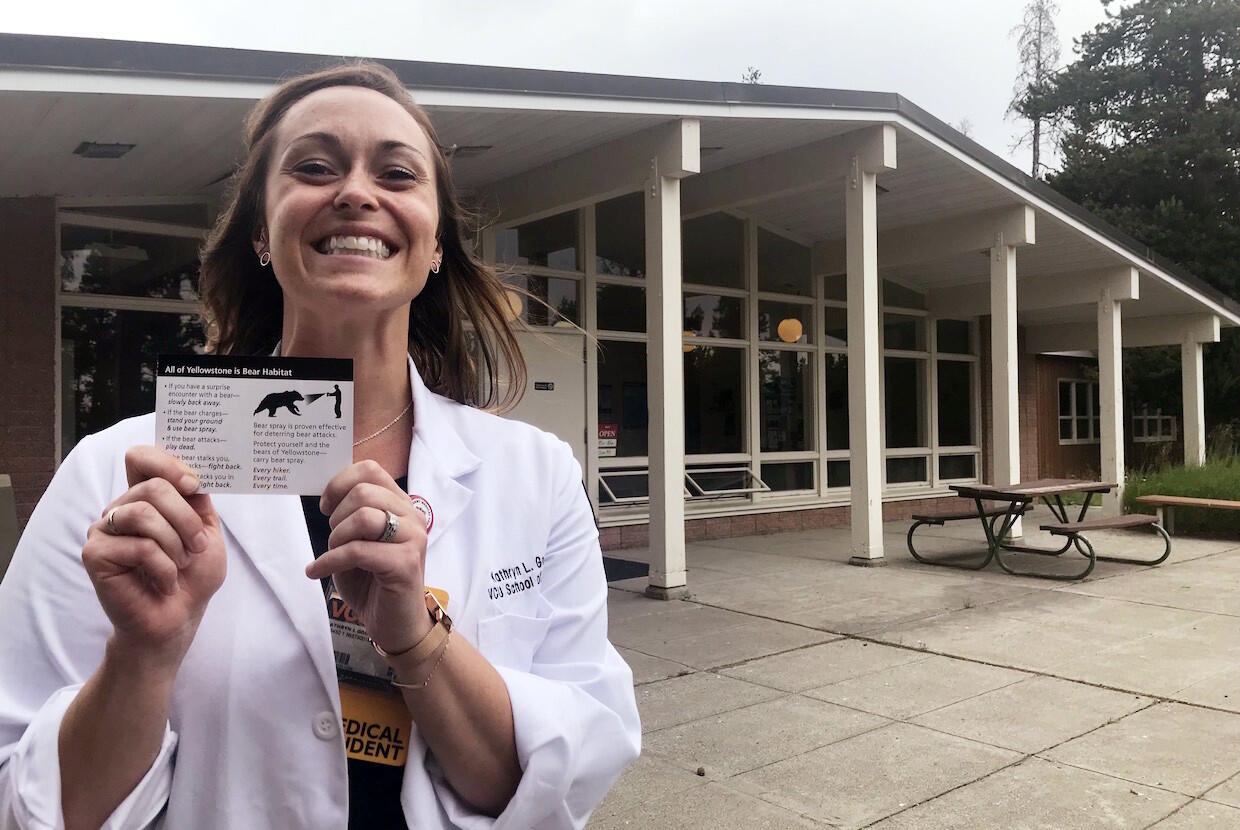 Woman in white doctor's coat holds a card with an image of a bear.