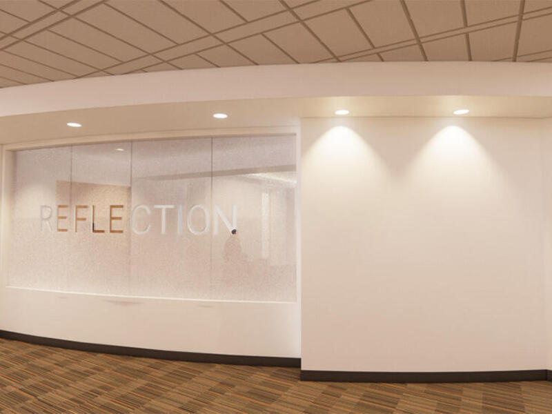 A white wall with a glass paneling that has the word \"REFLECTION\" written on in in white lettering. 
