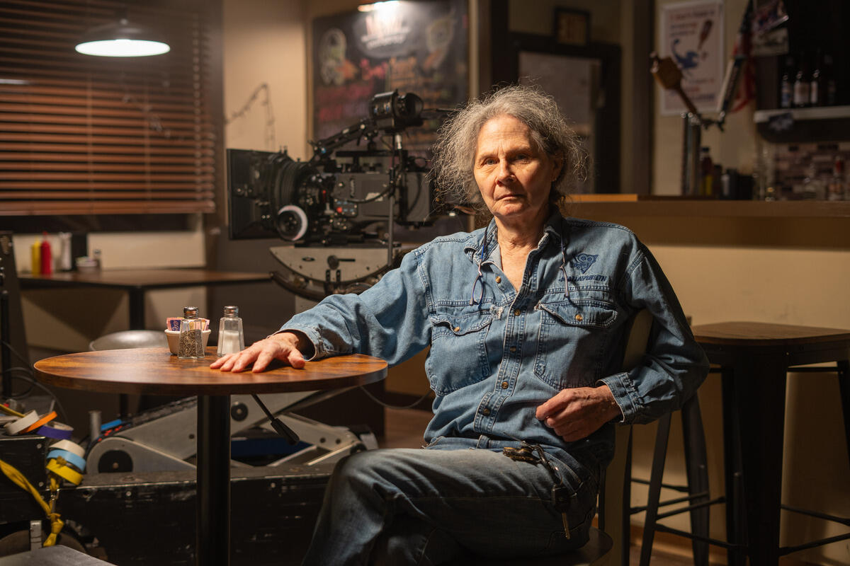 A photo of a man sitting at a table with a camera behind him. 