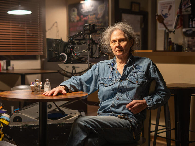 A photo of a man sitting at a table with a camera behind him. 