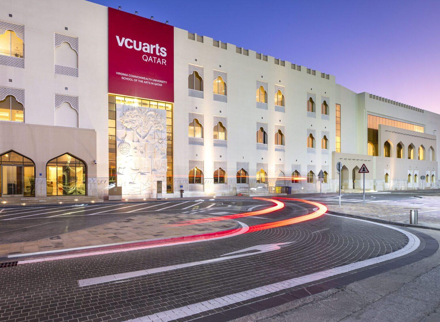 A long, low white building at dusk with vehicles parked out front.
