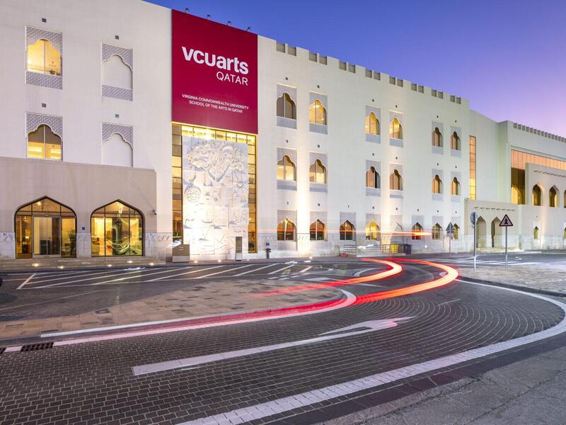 A long, low white building at dusk with vehicles parked out front.