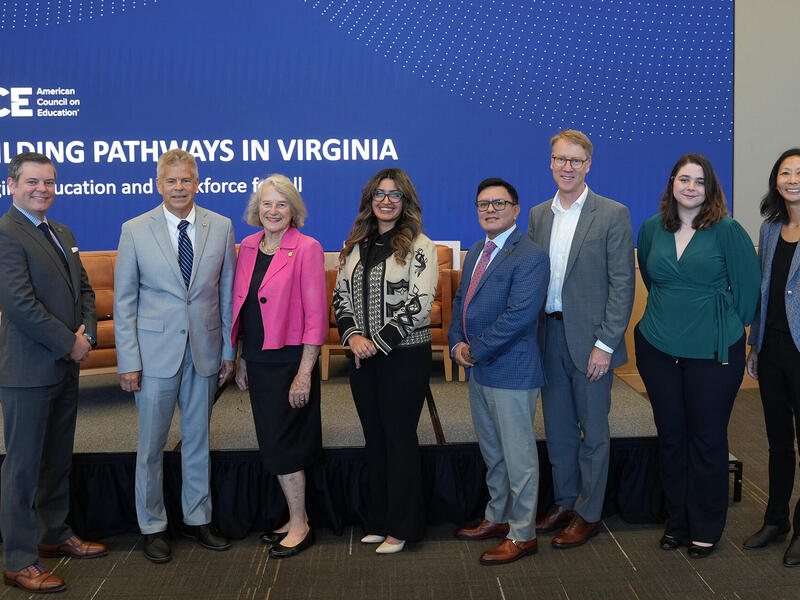 A row of eight people stand in front of a blue sign.