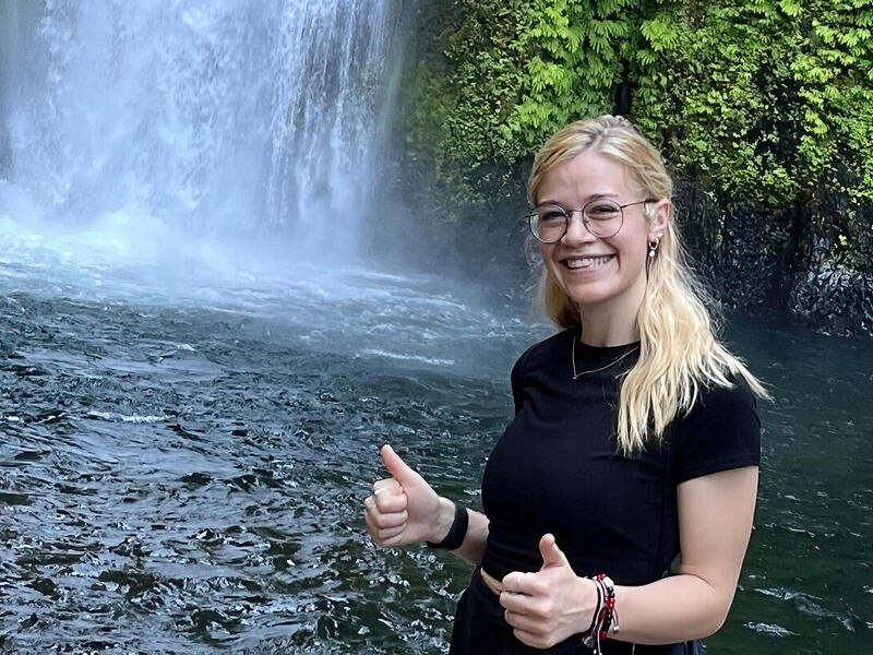 A woman standing in front of a waterfall giving two thumbs up. 