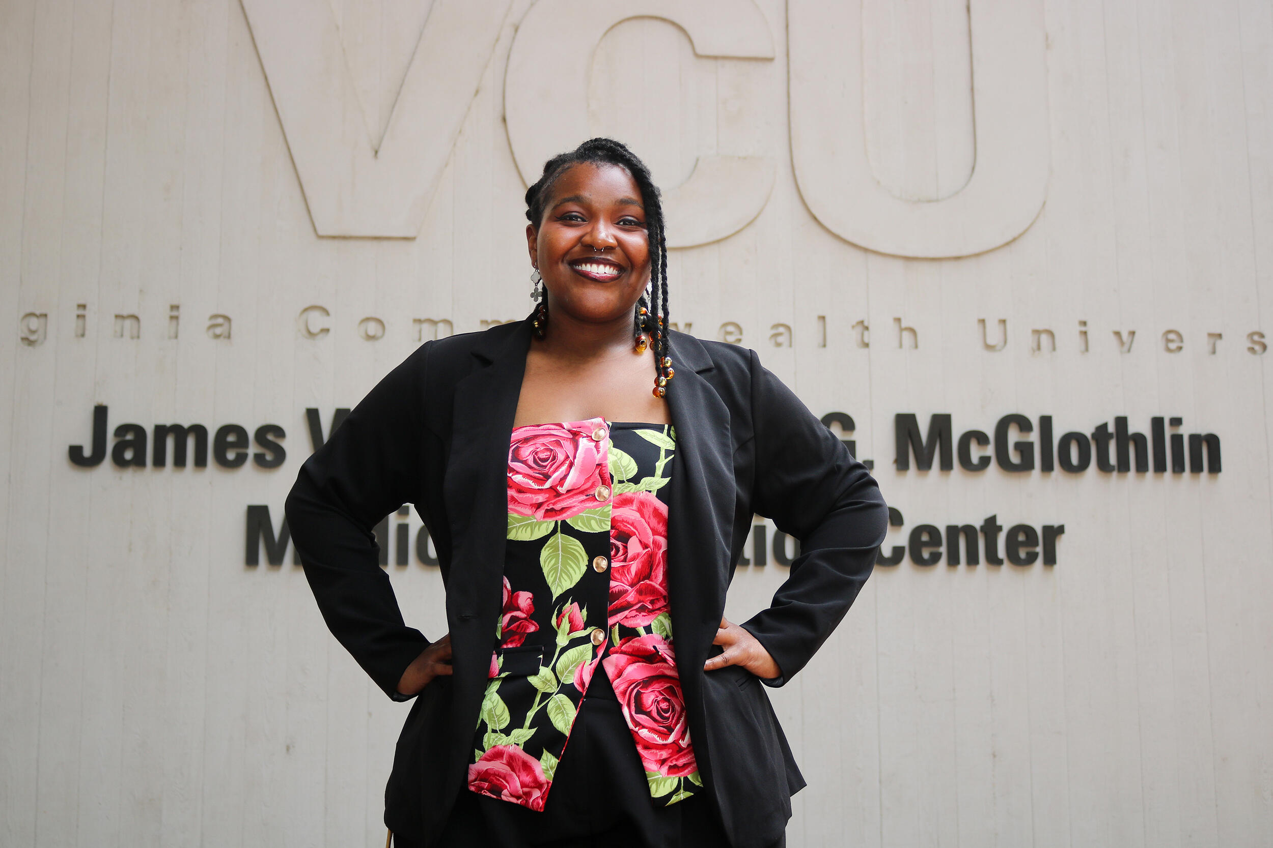 A photo of a woman from the waist up. She's standing with her hands on her hips. 
