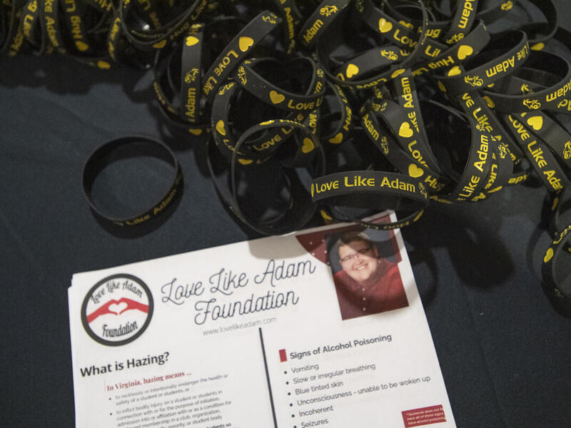 A photo of a card that says \"Love Like Adam Foundation\" next to a pile of black plastic bracelets that say \"Love Like Adam\" in yellow text. 