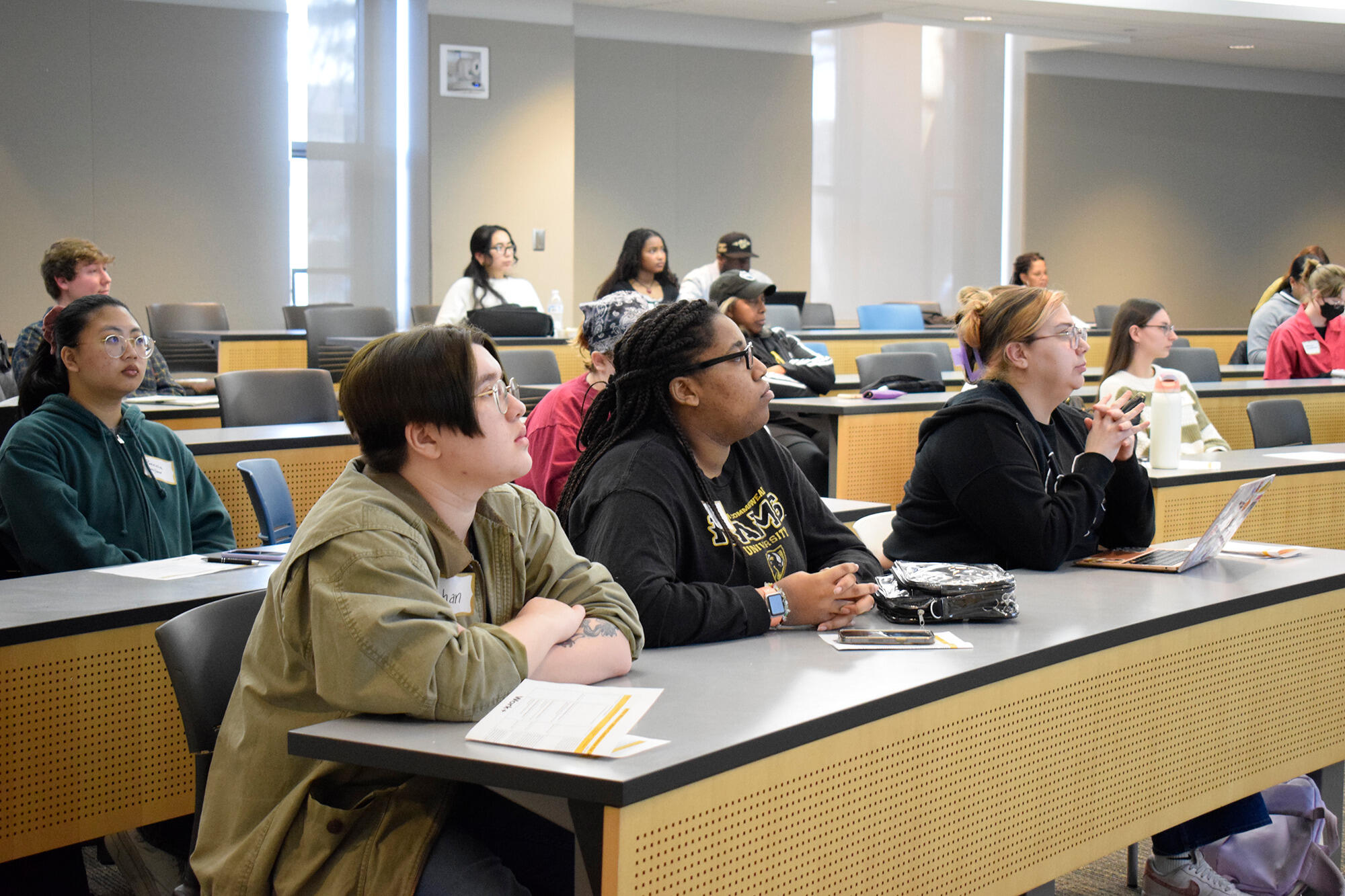 A photo of rows of desks and chairs. People are spread out throughout the rows sitting at the tables. 