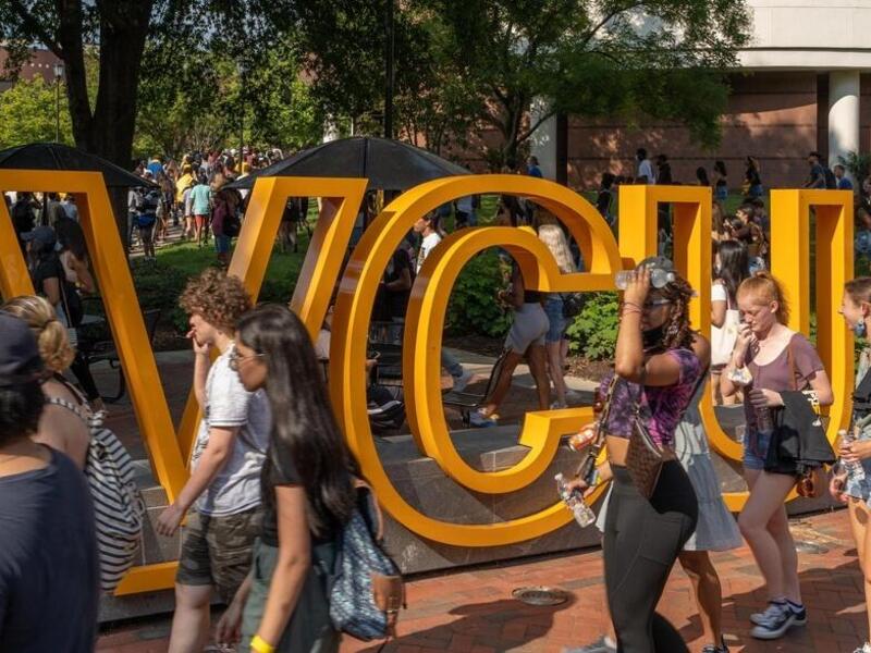 People walking past a sculpture of the letters \"VCU.\" 