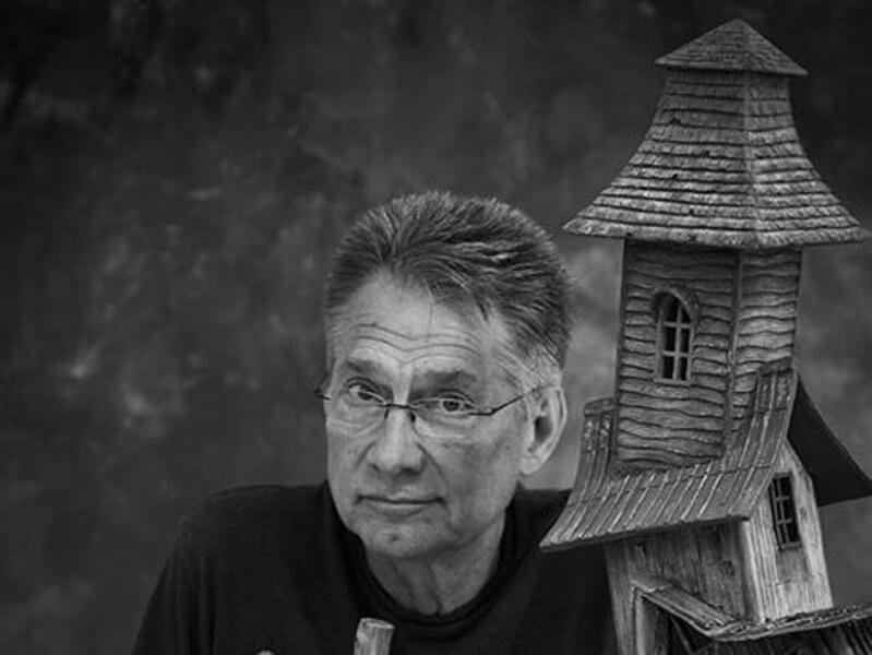 A photo of a man next to a model of an old abandoned house. 