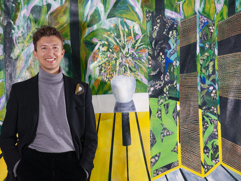 A man standing with his hands in his pockets in front of a colorful painting. 