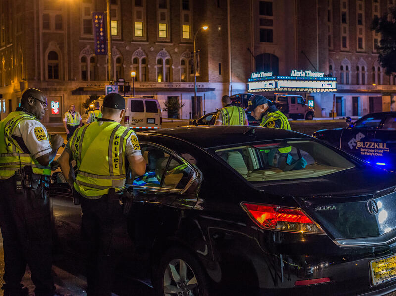 A photo of three police officers standing around a black car. 