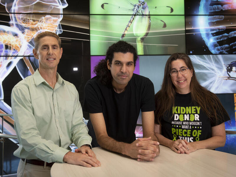A photo of two men and a woman standing next to each other behind a circular table. 