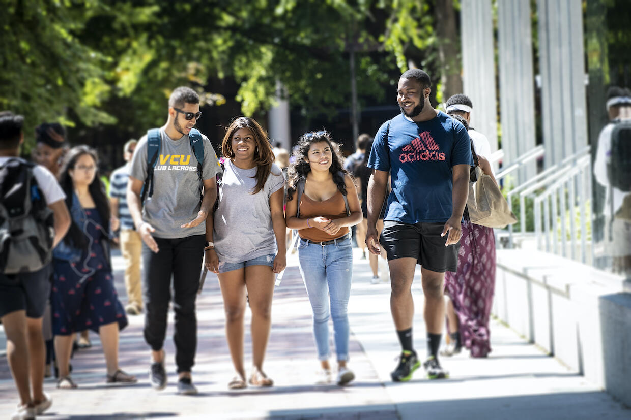 Four students walk side-by-side through campus. 