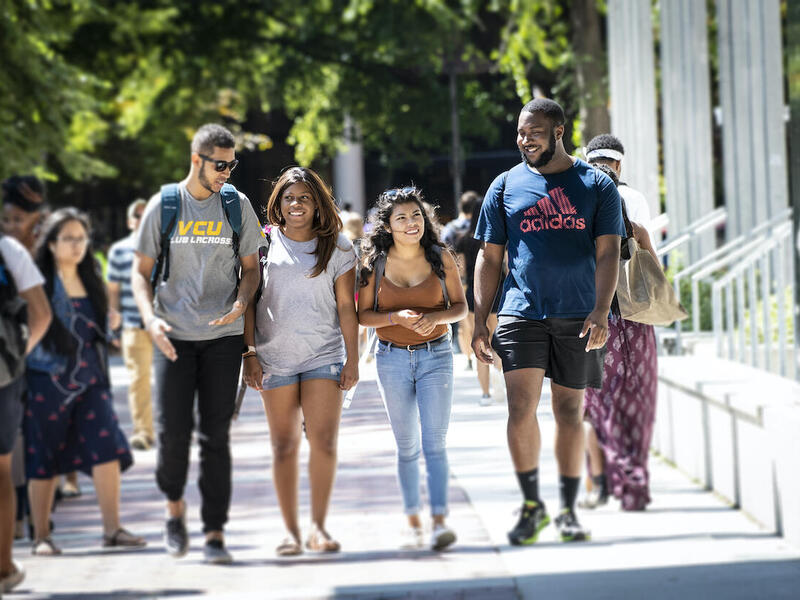 Four students walk side-by-side through campus. 