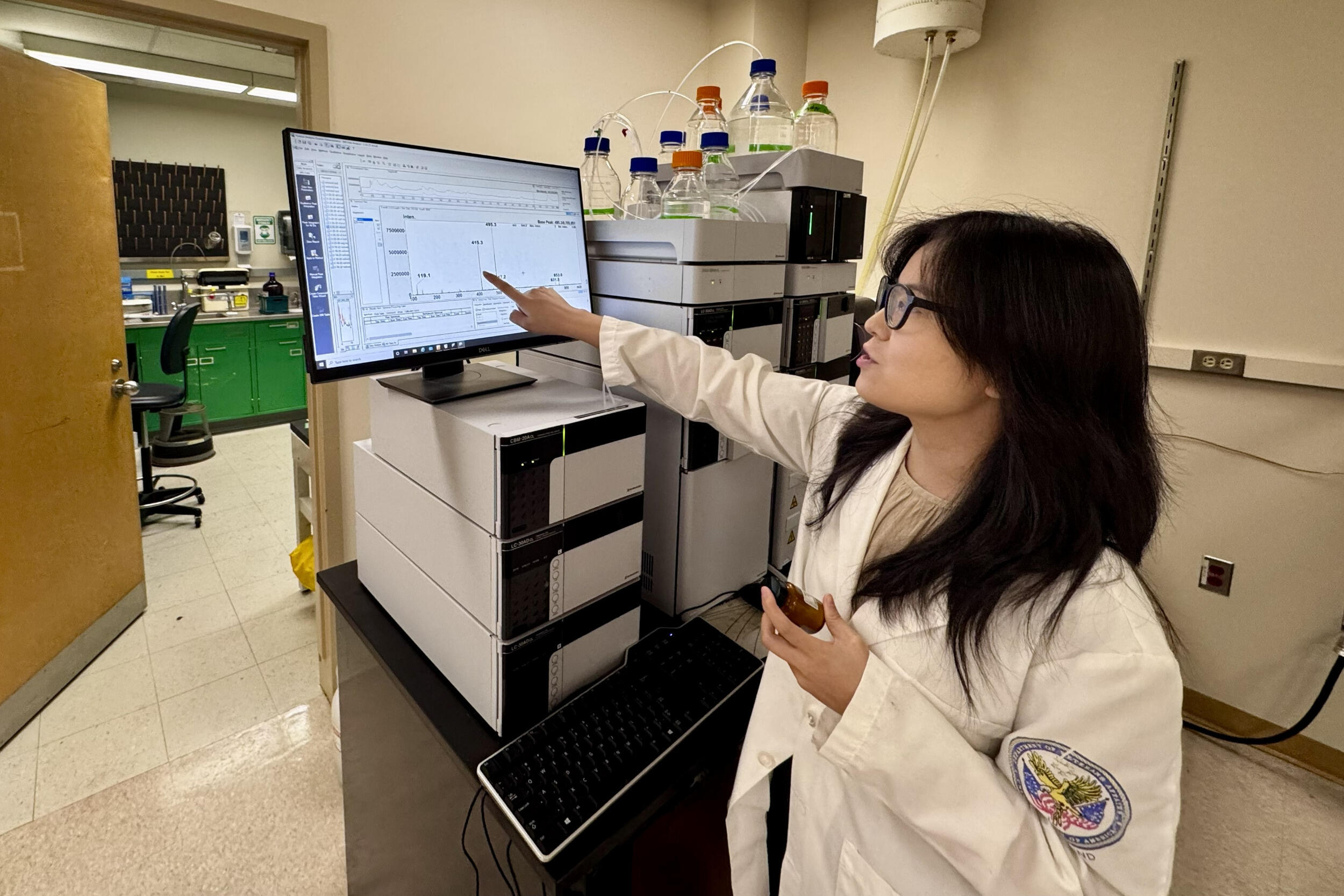 A woman in a lab coat points at a computer monitor.