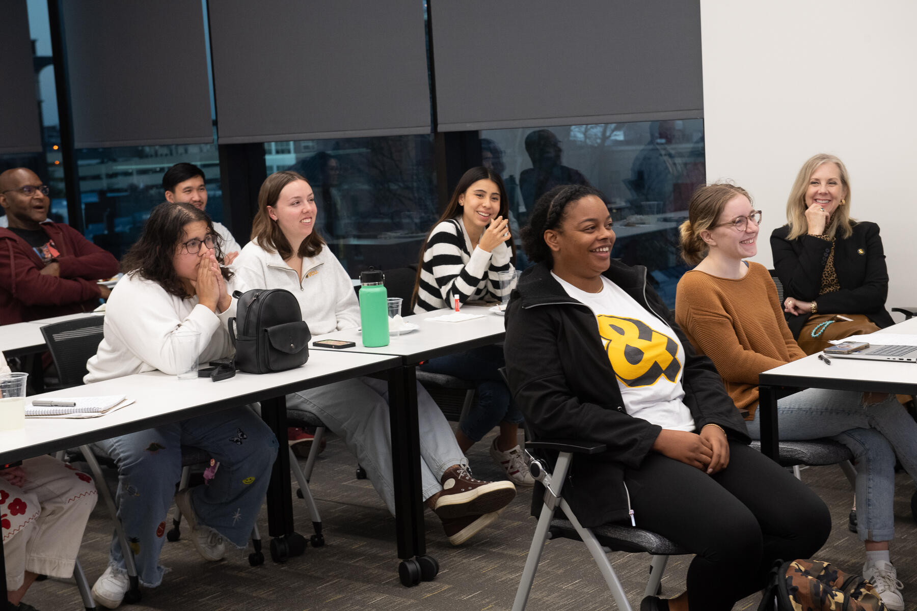 A photo of three rows of tables with people sitting at them. The first table has three people, the second table has three people and the thrid table has two people sitting at it. 