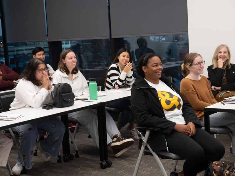 A photo of three rows of tables with people sitting at them. The first table has three people, the second table has three people and the thrid table has two people sitting at it. 