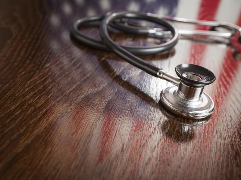 A stethoscope sitting on a wood table with an American Flag