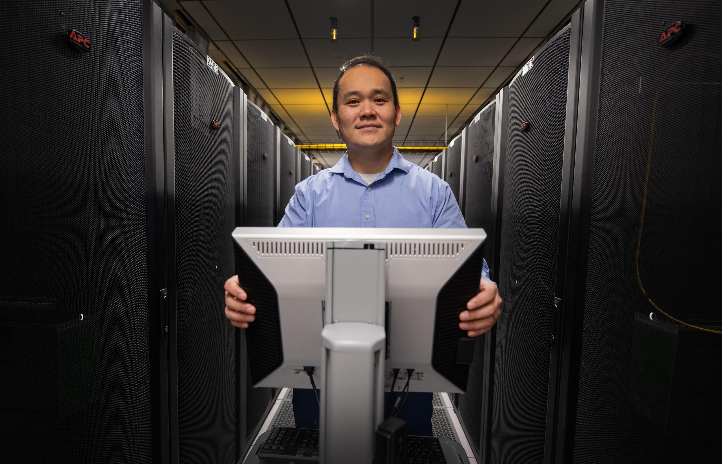 A photo of a man standing behind a computer monitor. 