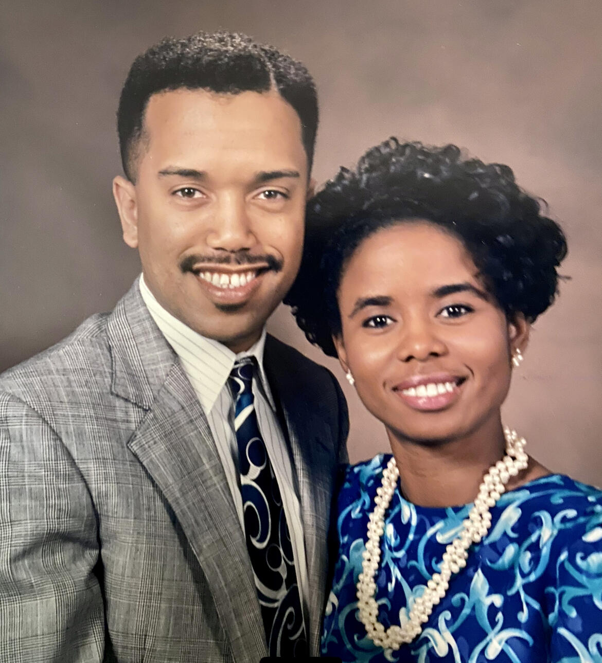 A man wearing a suit and tie standing next to a woman with a blue dress and pearl necklace 