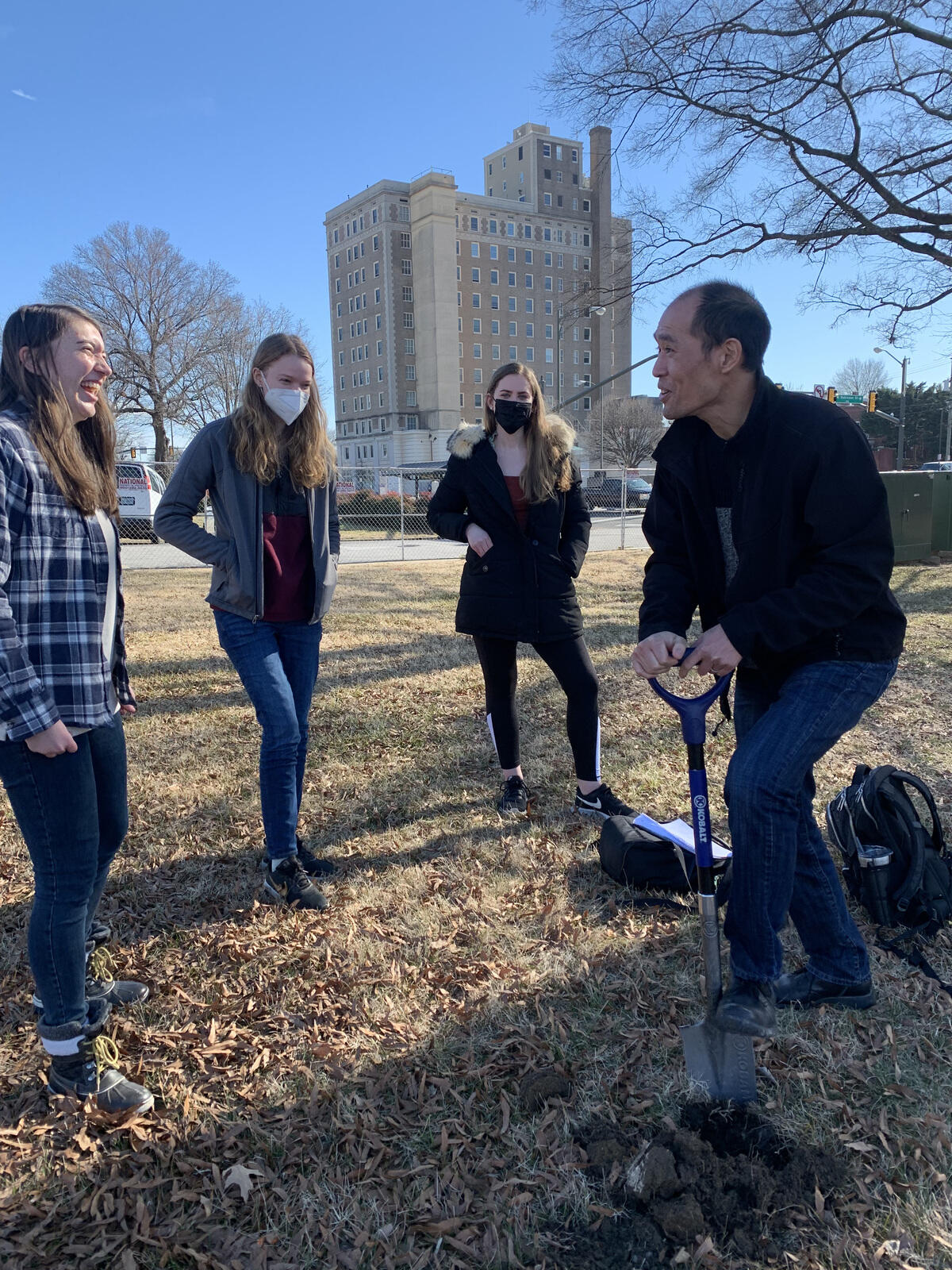 From left, students Emma Gregory, Alexandra Almasy and Tara Macintosh share a laugh with their professor Stephen Fong, Ph.D., as Fong digs into the ground in front of the Science Museum of Virginia.