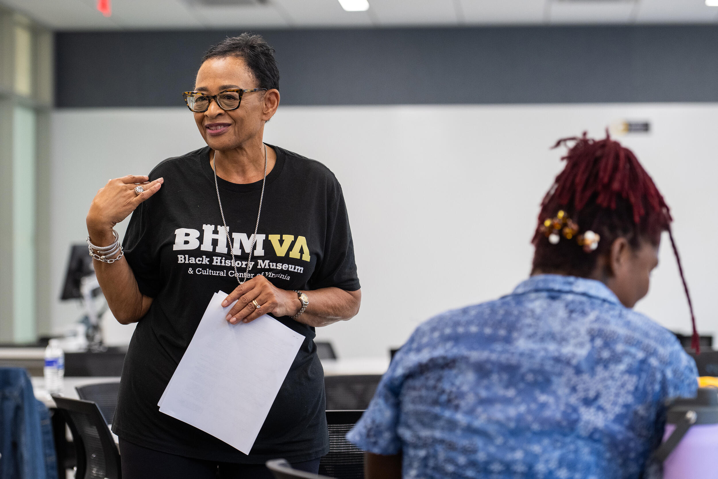 A photo of a woman standing in a room with a whiteboard behind her. In front of the woman is a teenager with her back to the camera. 