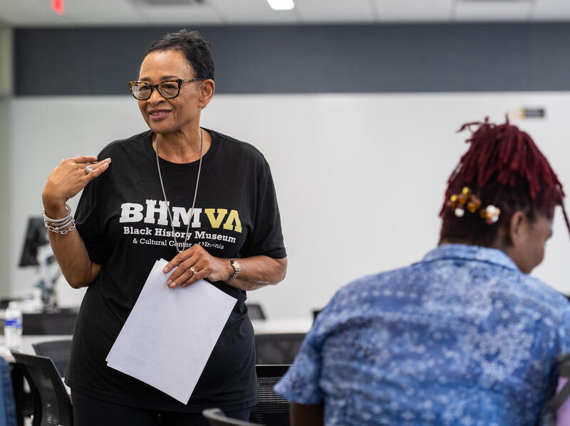 A photo of a woman standing in a room with a whiteboard behind her. In front of the woman is a teenager with her back to the camera. 