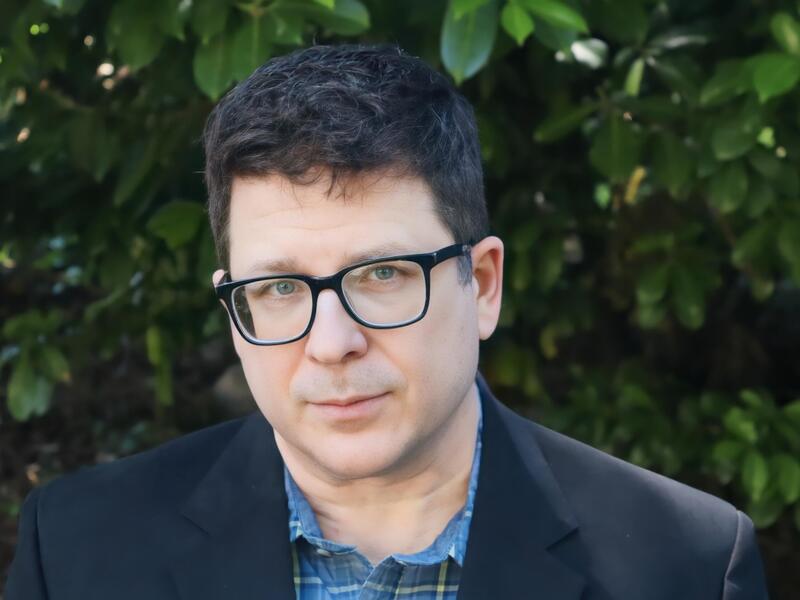 A photo of a man from the shoulders up. He is wearing glasses. 