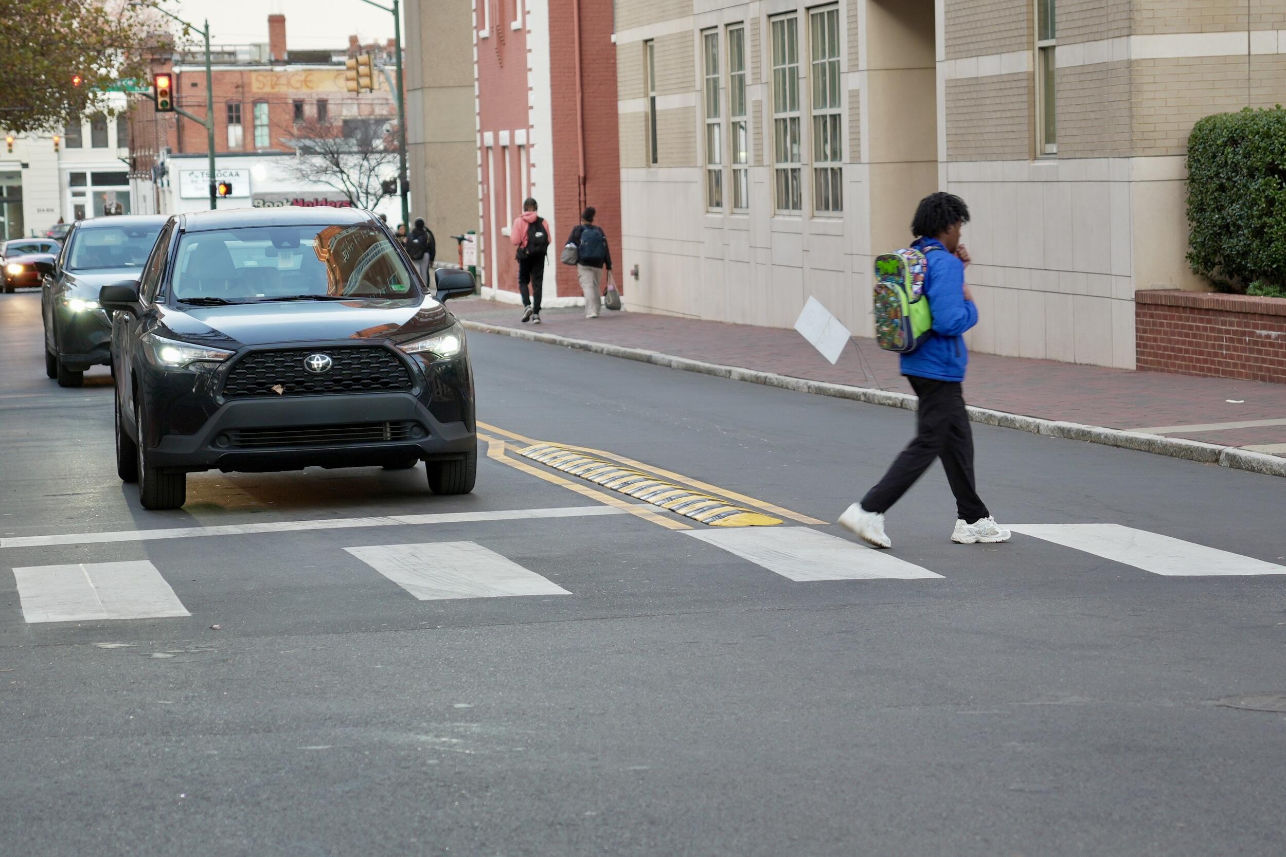 A photo of a person walking across a crosswalk where a car is stopped. 
