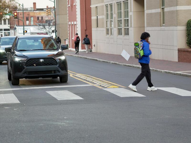 A photo of a person walking across a crosswalk where a car is stopped. 