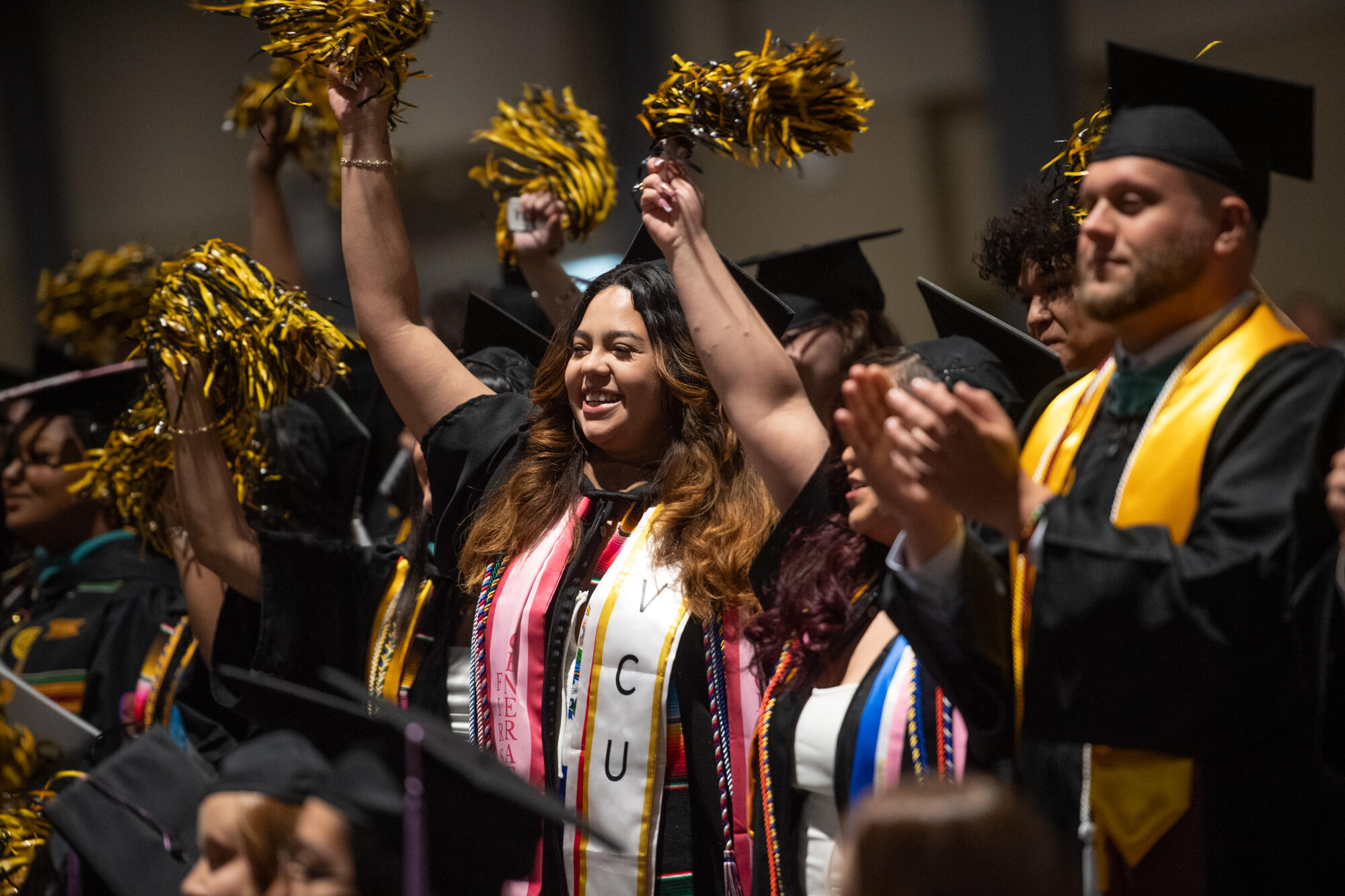 Students in caps and gowns wave pompoms during graduation.
