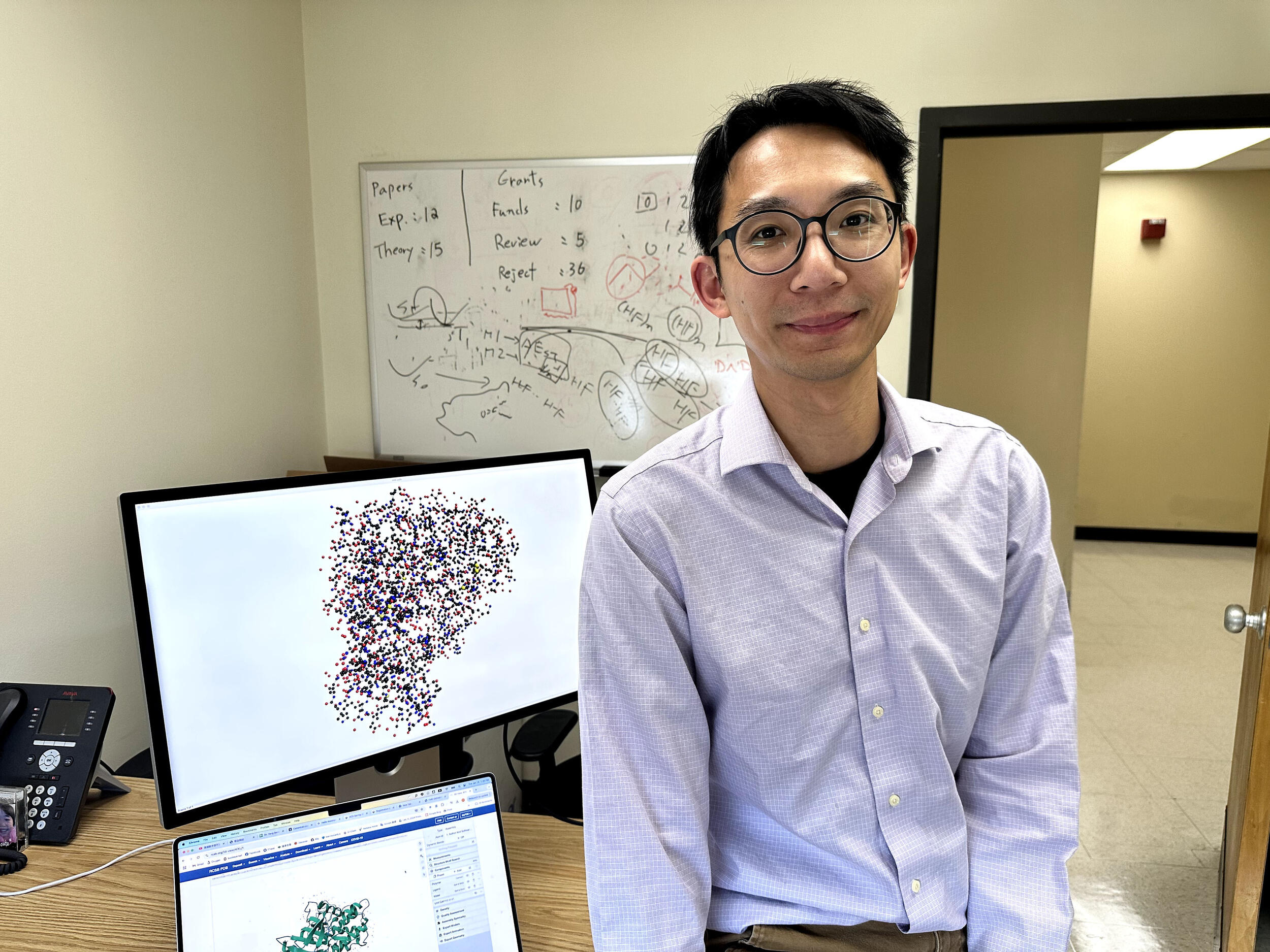 A photo of a man in front of a table with a laptop and computer monitor on it