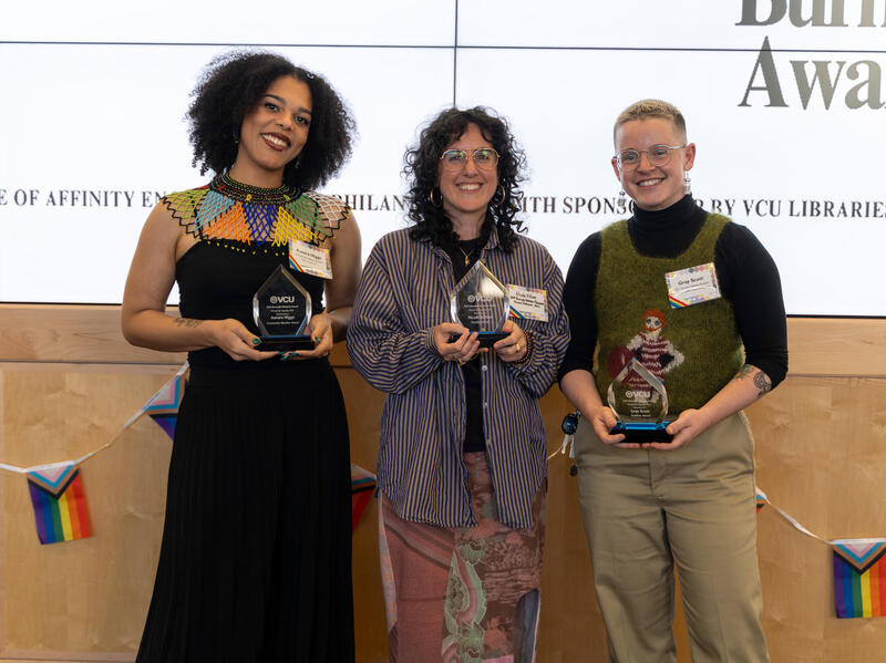 A photo of three people standing and holding glass trophies. 