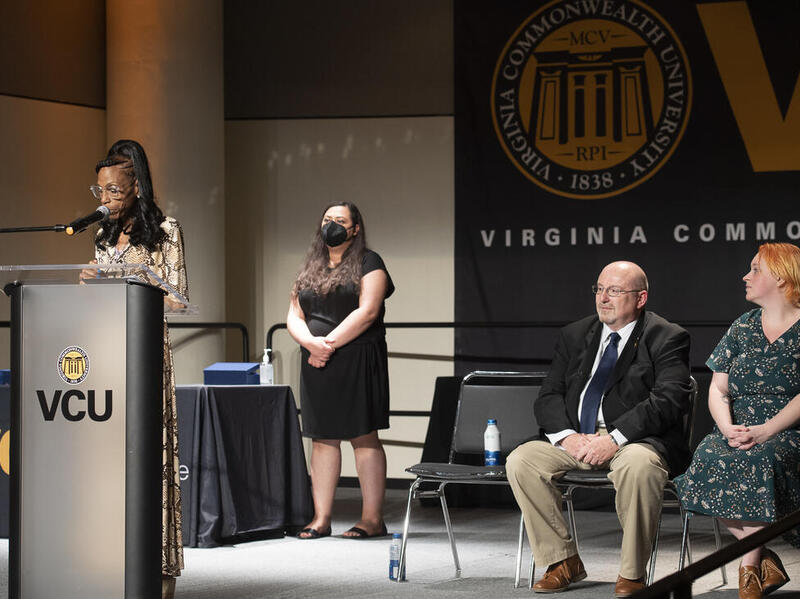 Michele Armstrong, a member of the VCU Staff Senate, speaks at last week's awards. Standing behind her is Saher Randhawa, president of the Staff Senate, and seated are Ken Hudgins, co-chair of the Awards & Recognition Committee, and Brogan King, co-chair of the Awards & Recognition Committee and president-elect for Staff Senate.