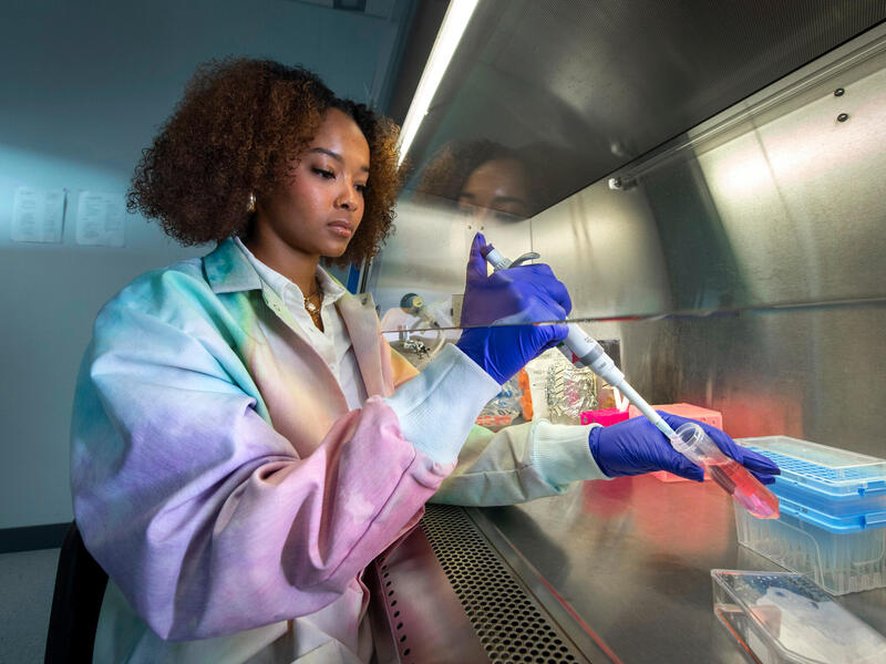 Student in a lab coat uses a pipette.