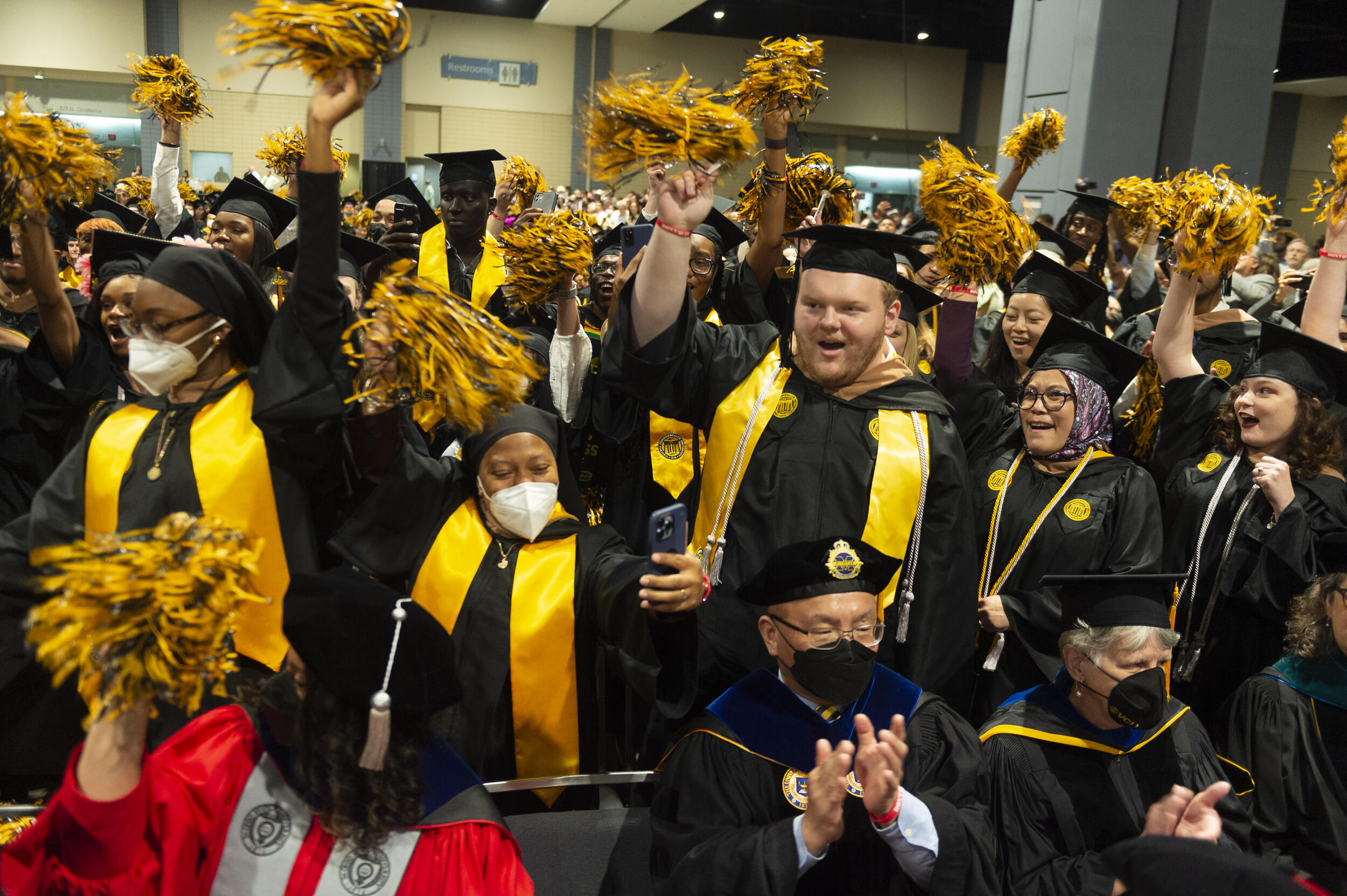 Students wearing caps and gowns waving black and yellow pom poms in the air. 