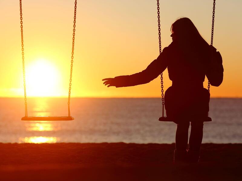 Woman on swing set reaches toward empty swing.
