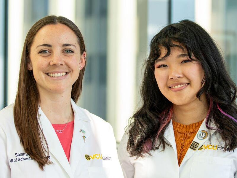 Two women wearing white lab coats standing in front of windows. 