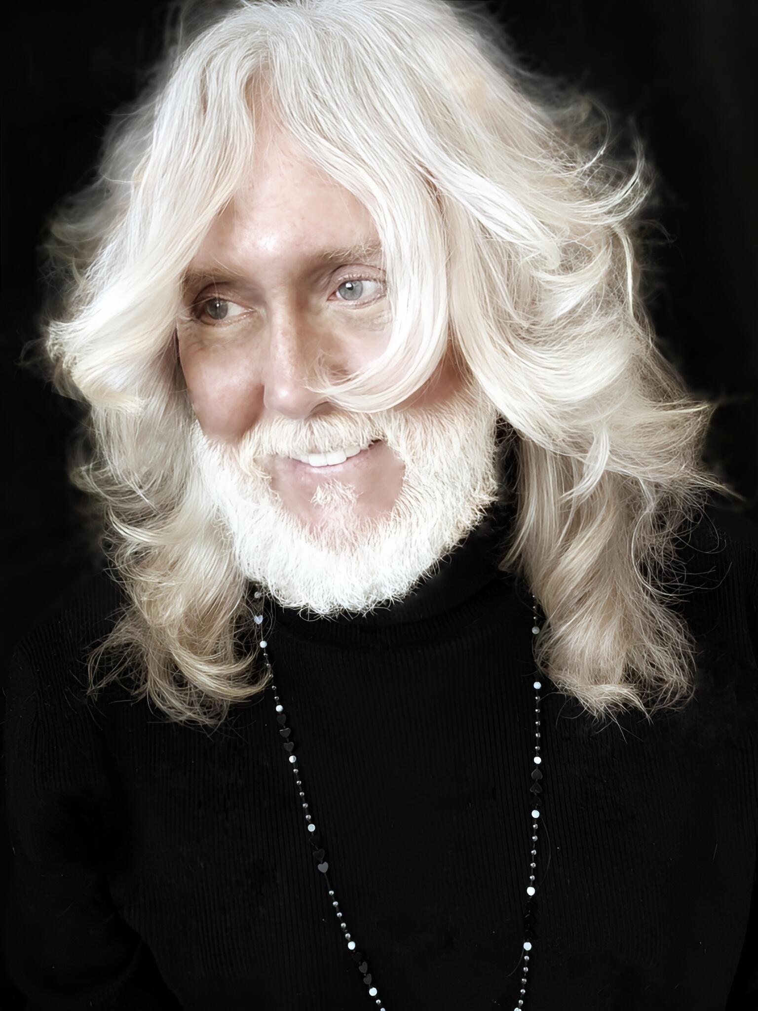 A photo of a man with white hair and a white beard from the chest up. 