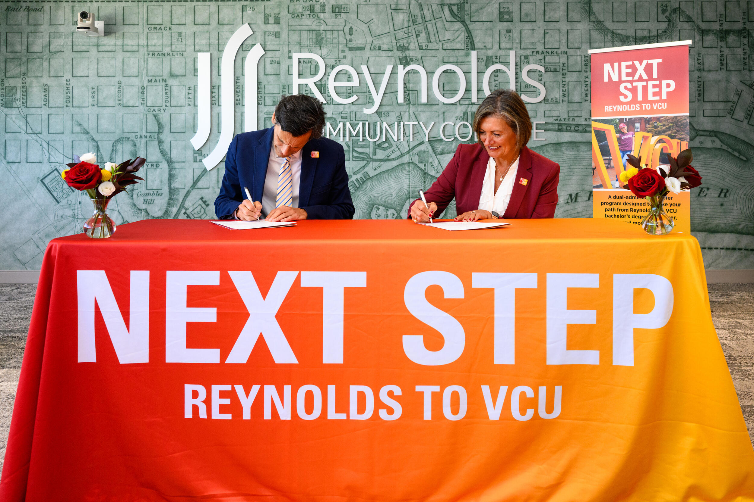 A photo of a man and woman sitting at a table signing documents. 