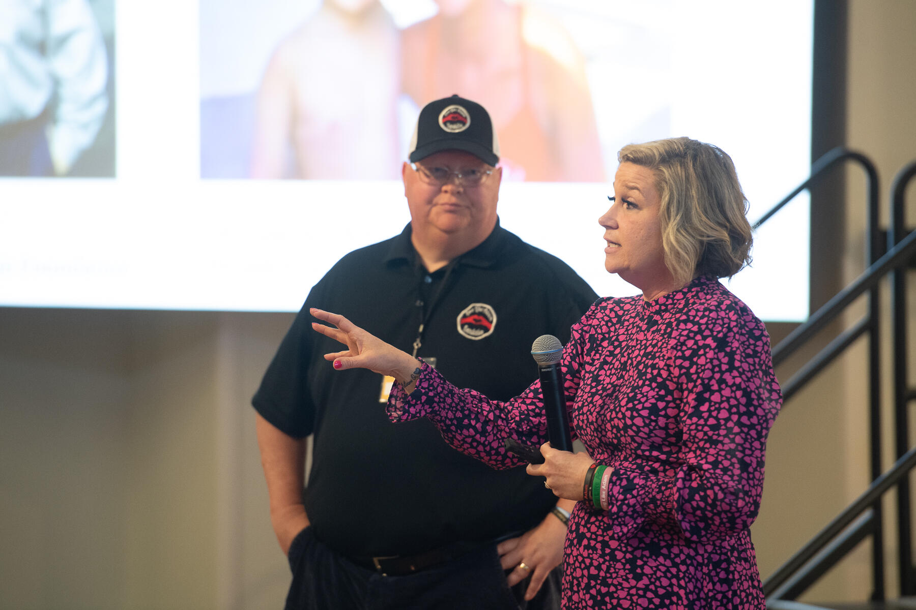 A photo of a man standing next to a woman who is holding a microphone and speaking. 