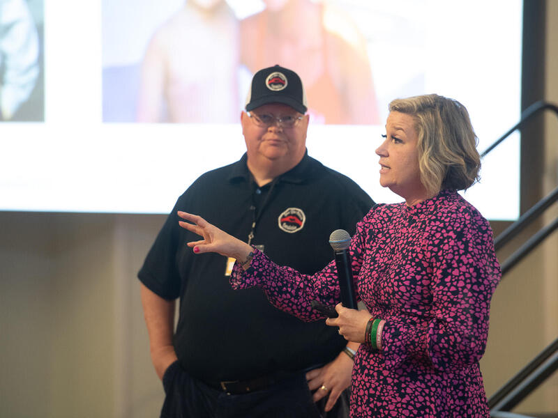 A photo of a man standing next to a woman who is holding a microphone and speaking. 