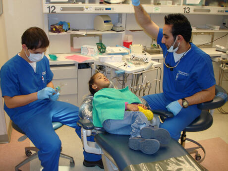 Nikolay Mollov prepares to clean Imarara Monclova’s teeth while Hasheem Ghadhanfari adjusts the light.
