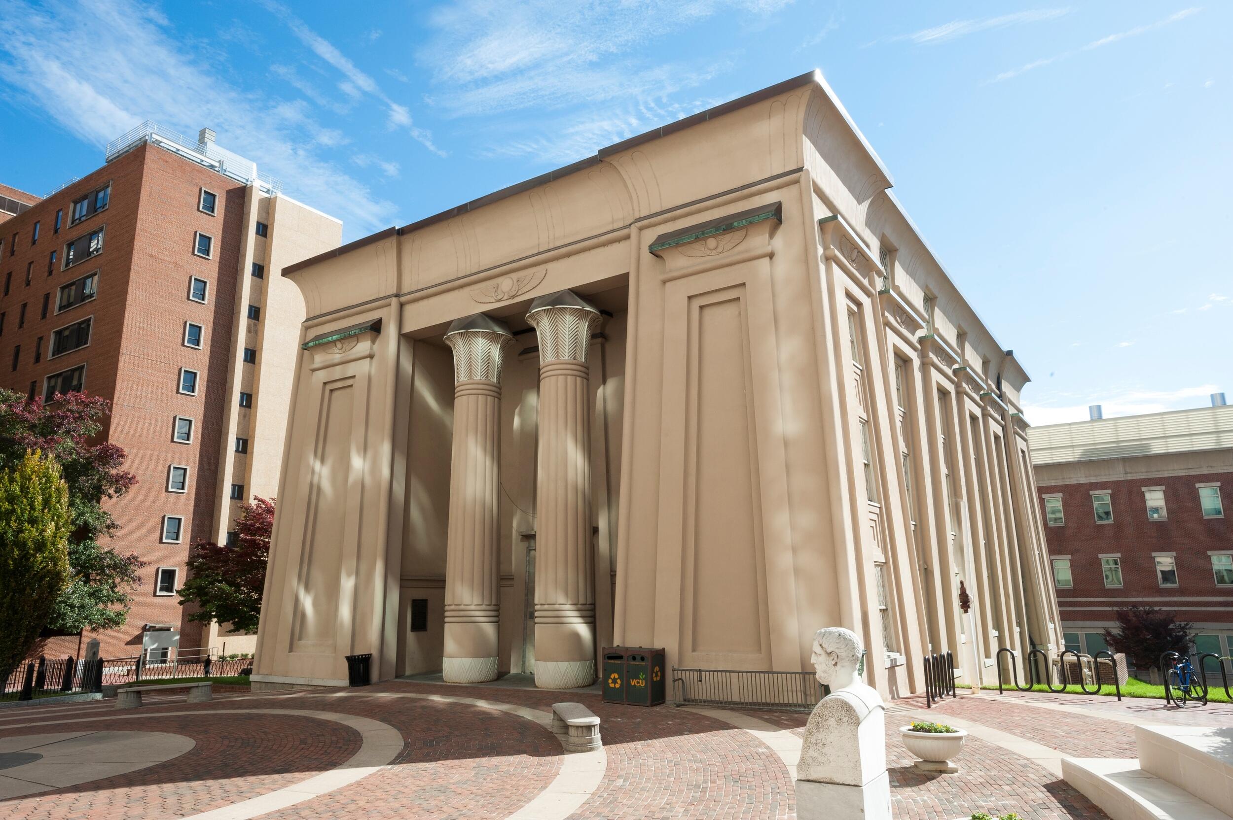 Exterior of a building with two prominent columns and a courtyard in front of it.