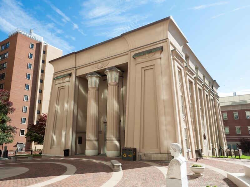 Exterior of a building with two prominent columns and a courtyard in front of it.