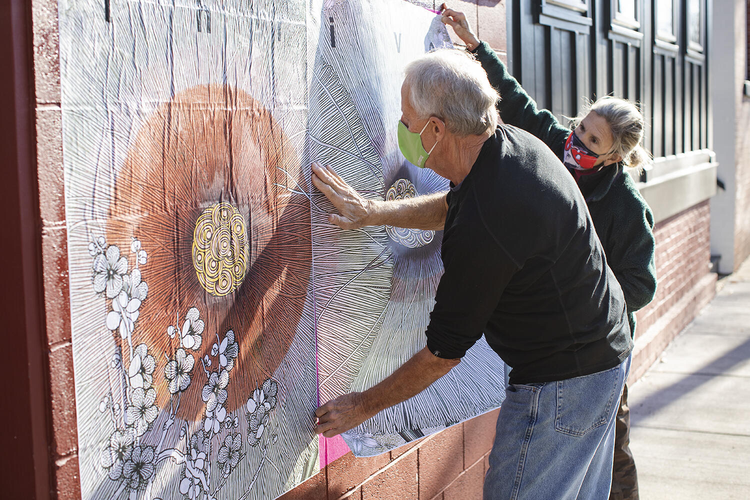 Two people affix a poster to a brick wall 