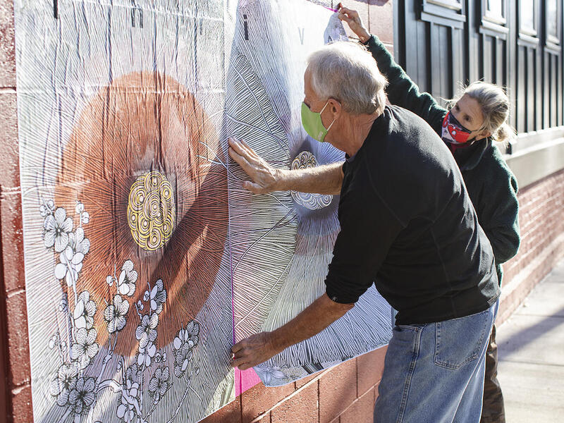 Two people affix a poster to a brick wall 
