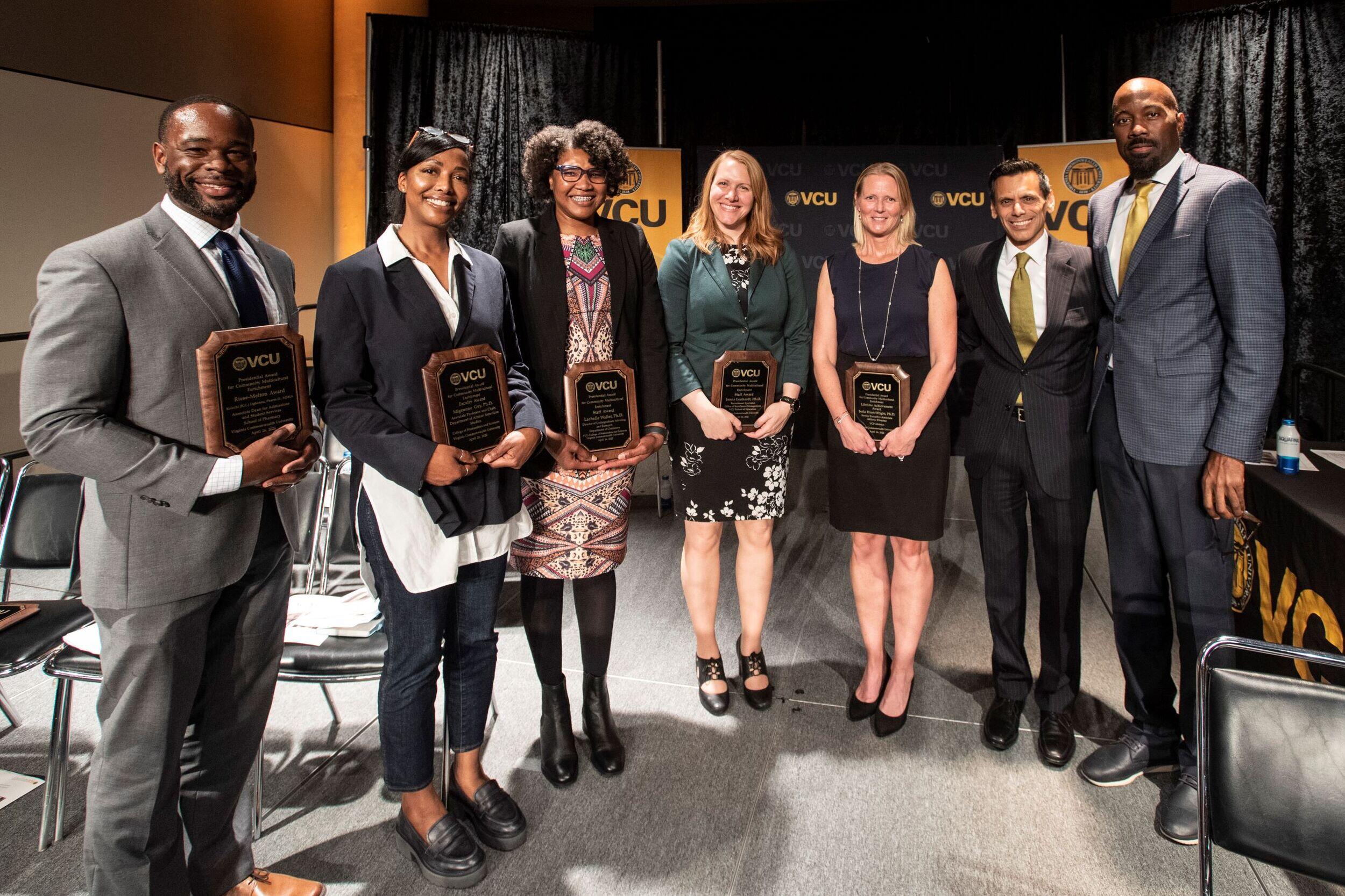 Five award winners lined up holding their plaques with two others joining them.
